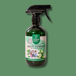 A dark green glass spray bottle of Living ELL Multi-Purpose Natural Cleaning Spray with a black trigger sprayer, set against a solid sage green background.